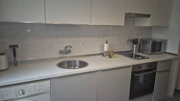 A kitchen with a washing machine, a microwave, a sink, and cabinets.