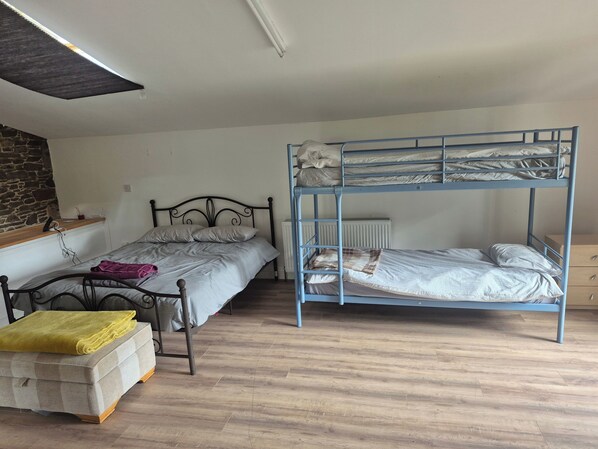 A room with two single beds, a bunk bed, a small wooden table, and a stone wall. - Bellhouse Hassendeanburn- Sleeps 10 hot tub (Hawick)