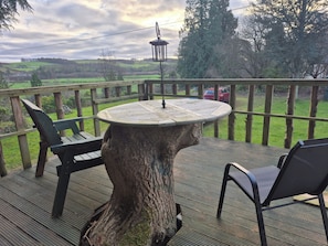 A deck with a round table and chairs, surrounded by a wooden railing, overlooking a green landscape. - Bellhouse Hassendeanburn- Sleeps 10 hot tub (Hawick)
