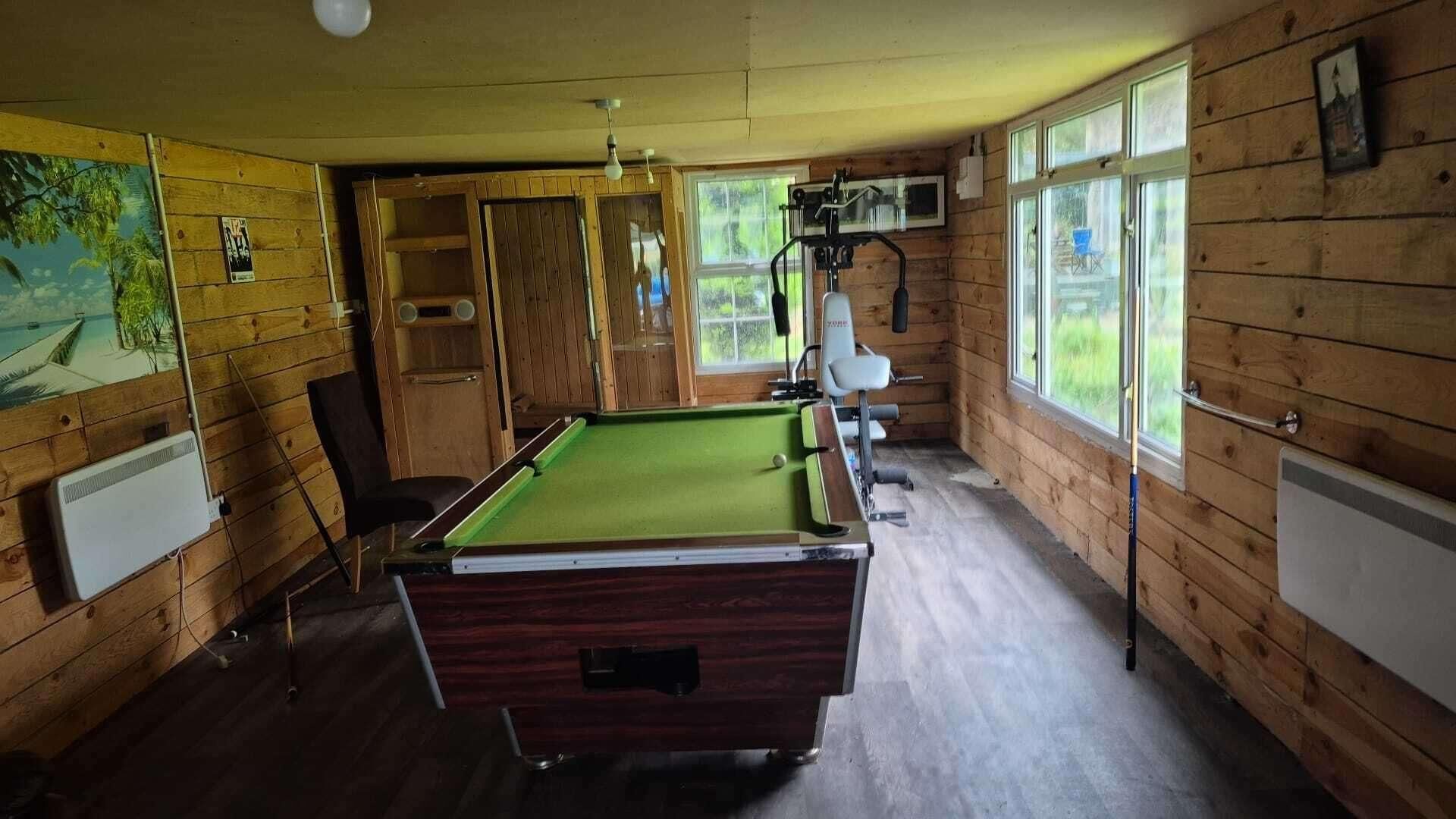 Una mesa de billar en una sala con paredes de madera, una ventana y una puerta.