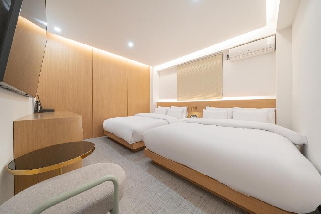 A modern hotel room with a large bed, bedside tables, a flat-screen TV, and an air conditioning unit.