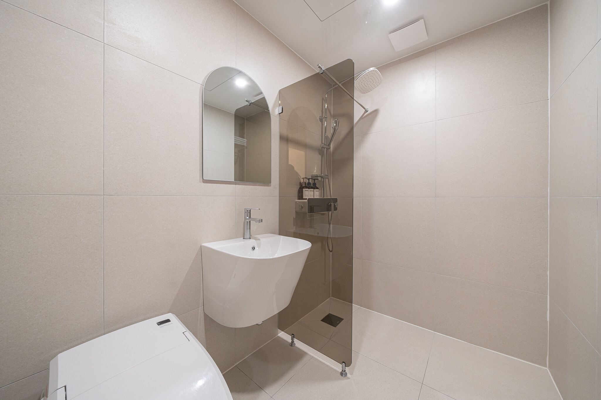 Un baño moderno con lavamanos blanco, ducha con cerramiento de vidrio y espejo sobre el lavamanos.
