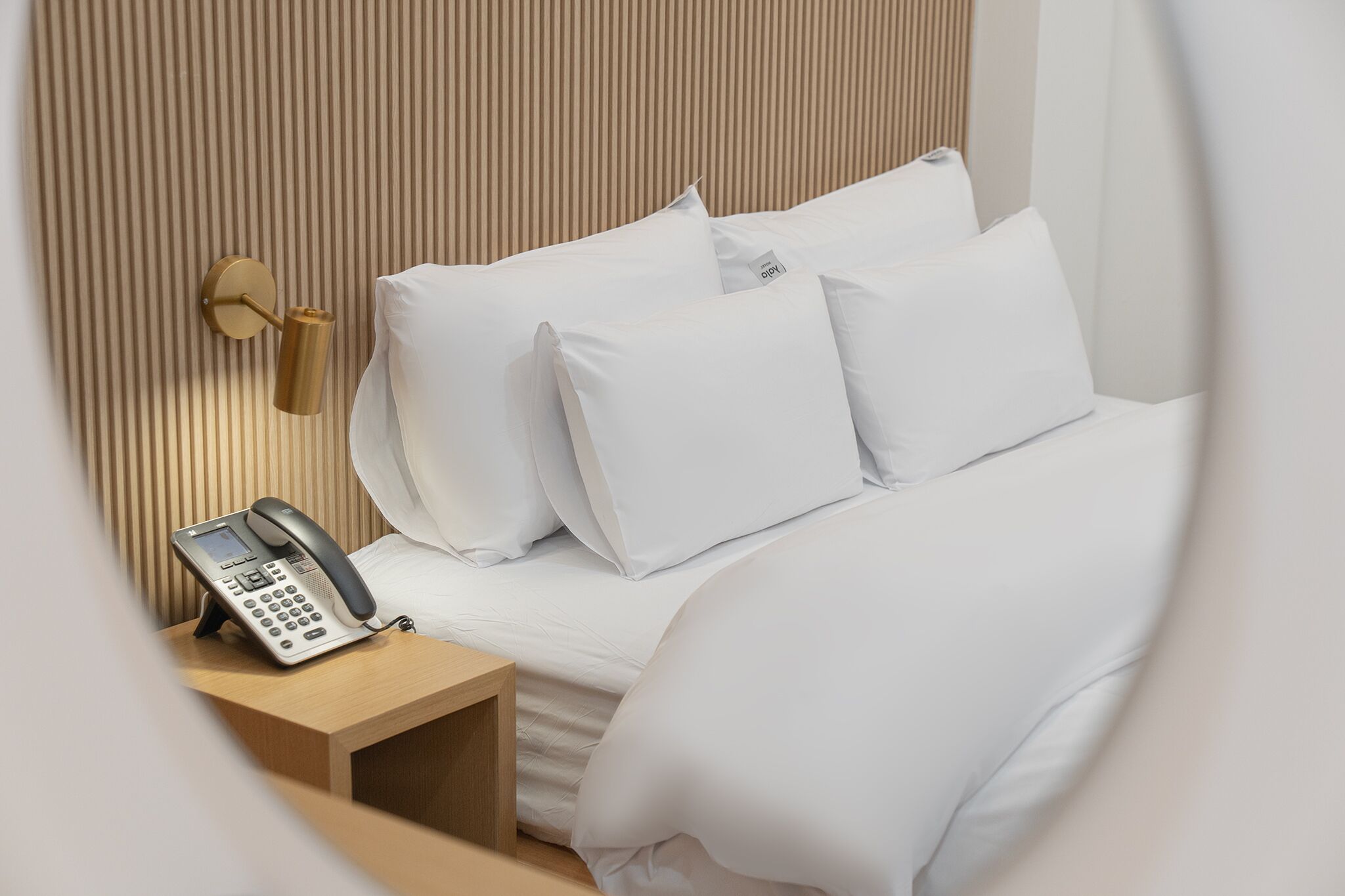 Una cama bien tendida con sábanas blancas y un teléfono en una mesita de noche de madera.