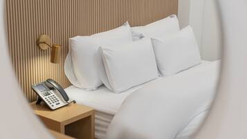 Una cama bien tendida con sábanas blancas y un teléfono en una mesita de noche de madera.