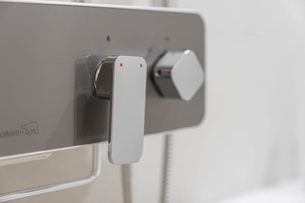 Un baño moderno con un grifo metálico elegante y un panel de control.