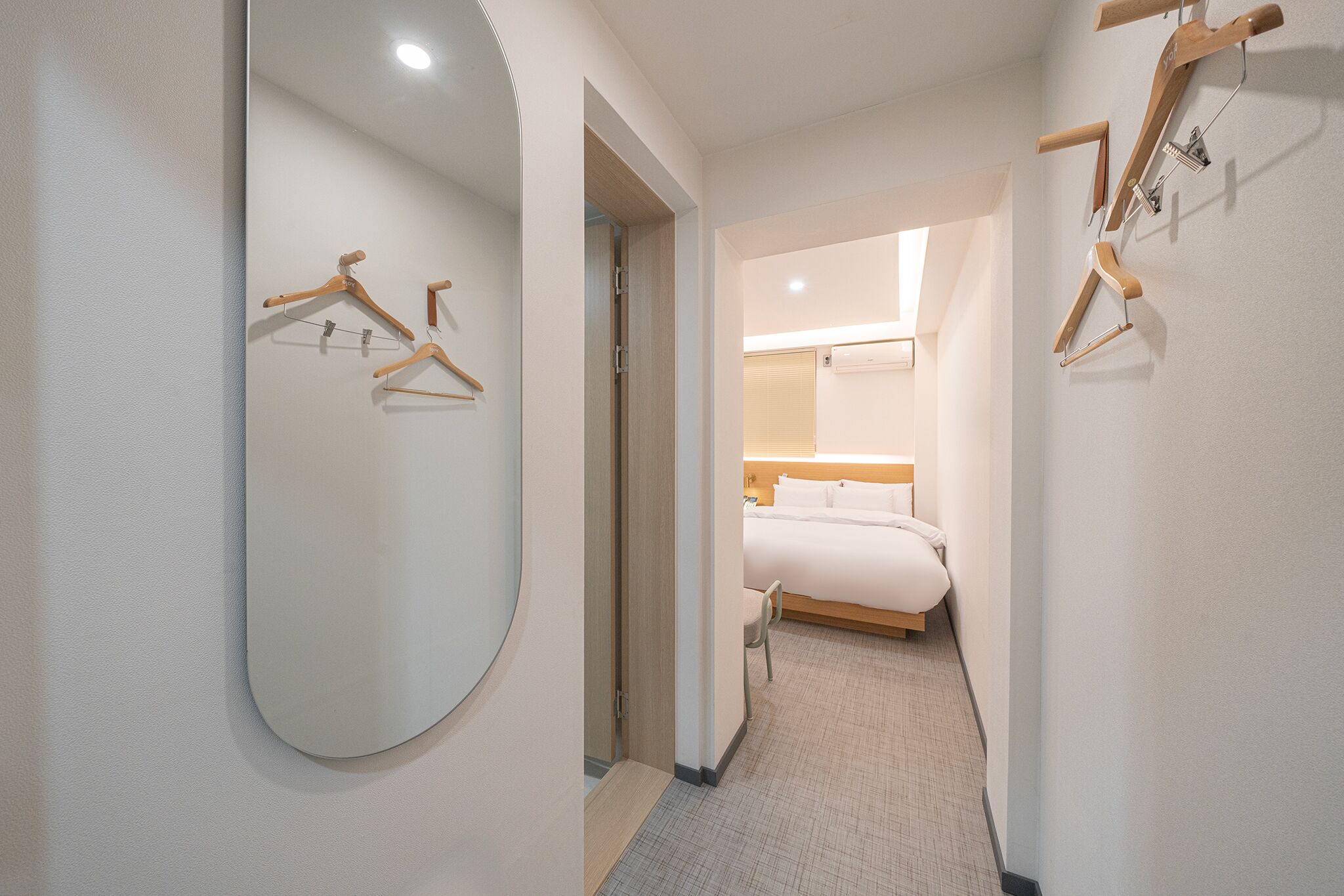 A hotel room with a large mirror, wooden hangers, a bed, and a small table.