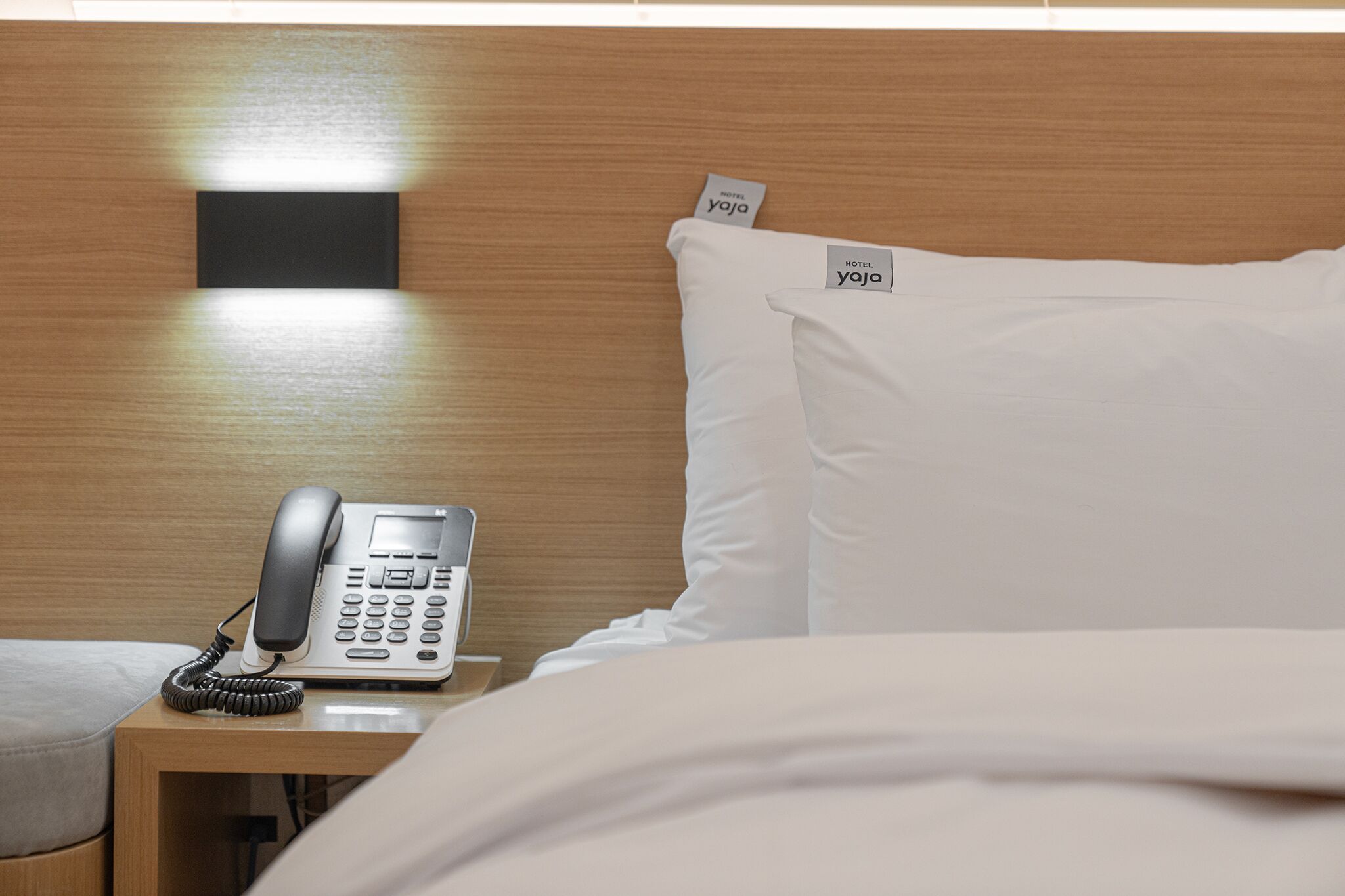 Ein Hotelzimmer mit Nachttischtelefon, Kissen und einem Schild mit dem Hotelnamen.
