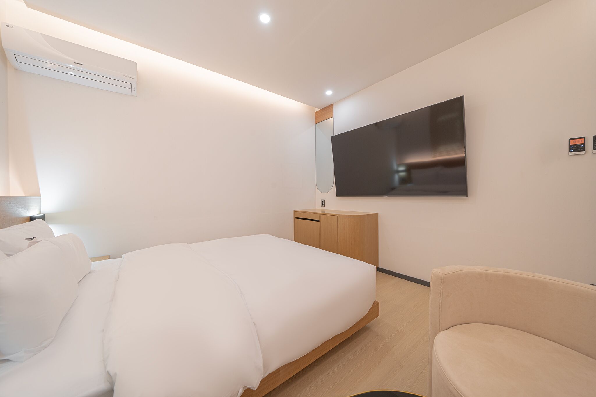 A modern hotel room with a bed, a bedside table, a TV mounted on the wall, and a small seating area.