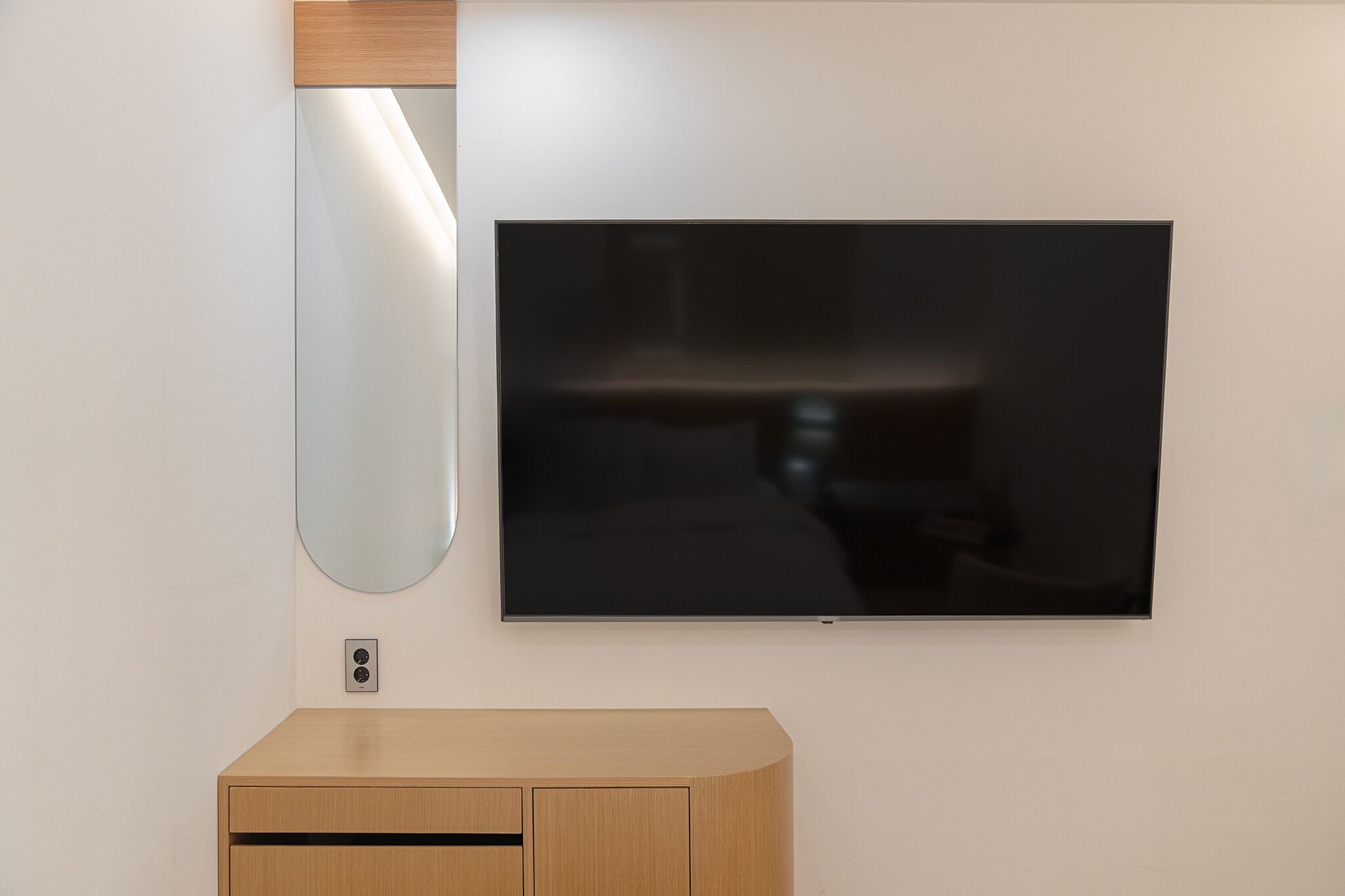 Ein modernes Zimmer mit Flachbildfernseher an der Wand, einem Holfach darunter und einer Wandleuchte.
