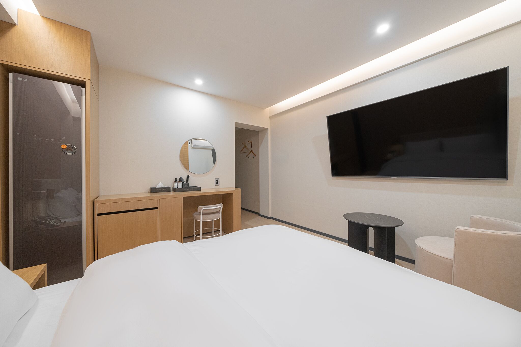 Una habitación de hotel moderna con una cama, un escritorio con una silla, un televisor montado en la pared y un armario.