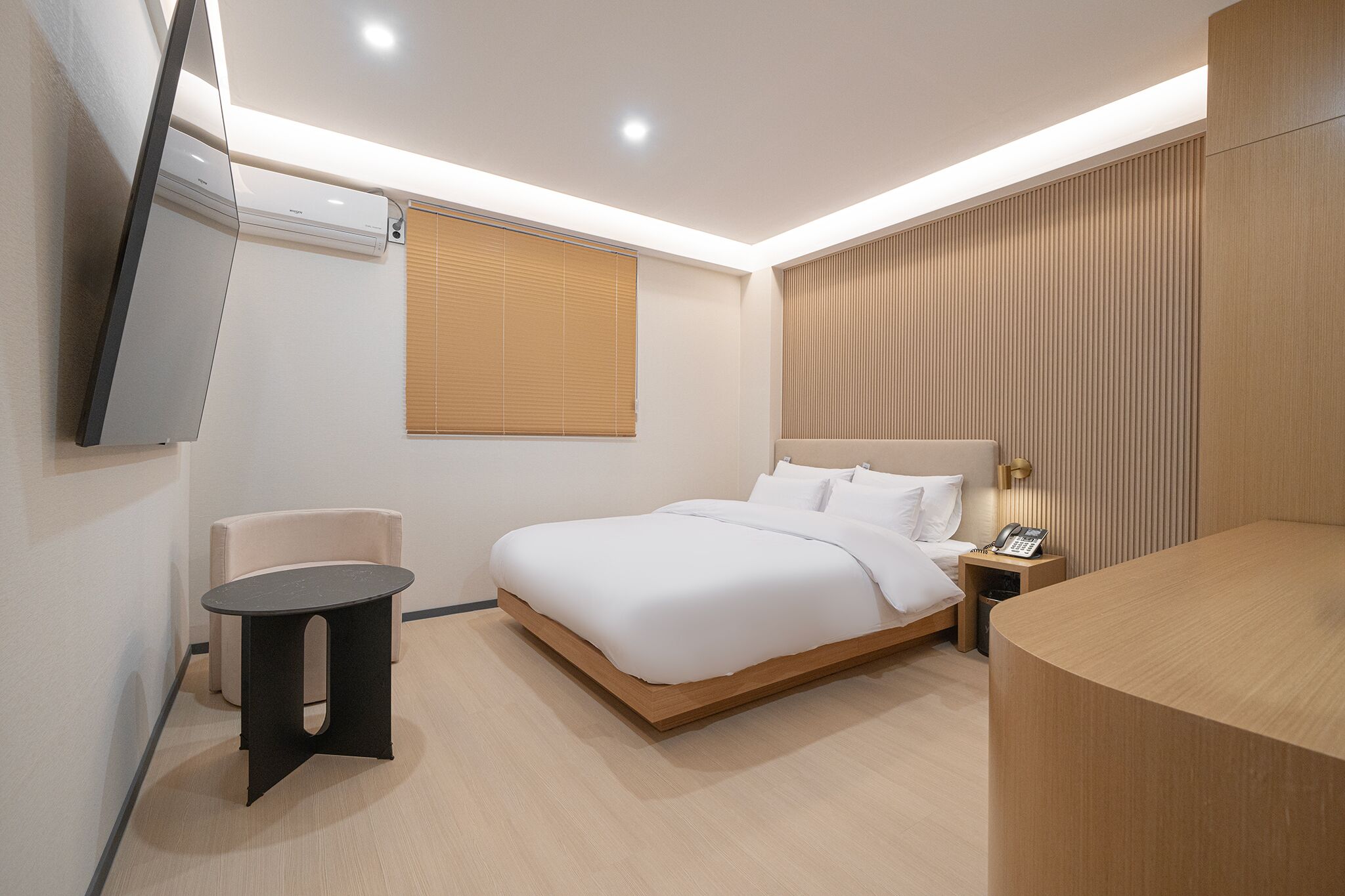 A modern hotel room with a large bed, bedside table, and a small seating area.