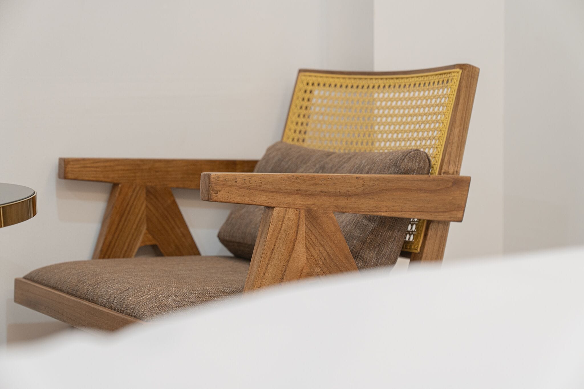 A wooden chair with a woven backrest and a cushion, placed in a room with a white wall and a small round table.