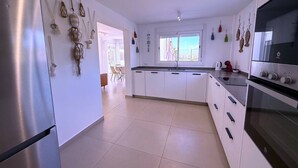 A modern kitchen with white cabinets, stainless steel appliances, and decorative wall hangings. - Villa Modern Princess (Golf Del Sur)