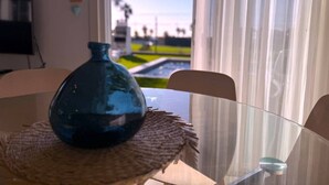 Una stanza con un tavolo in vetro, un vaso azzurro e vista su un paesaggio verde attraverso una finestra con tende leggere.