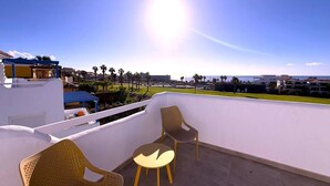 Una terrazza sul tetto con due poltrone in vimini e un tavolino, con vista su una zona costiera con edifici e palme.