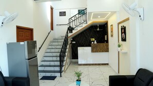 A hotel lobby with a reception desk, a staircase, a refrigerator, and two sofas. - Cloud9 Airport Hotel (Aluva)