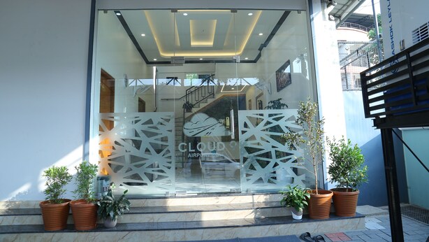 A modern building entrance with glass doors, potted plants, and a visible staircase leading inside. - Cloud9 Airport Hotel (Aluva)