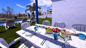 A dining table set with plates, cutlery, glasses, and a bowl of fruits and pastries, with a pool and lounge chairs in the background. - Villa  Red Princess - Private Heated Pool (Golf Del Sur)