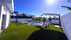 A rooftop pool area with artificial grass, sun loungers, and a clear blue sky. - Villa 6- Pink Princess (Golf Del Sur)