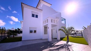 A modern two-story house with a flat roof, a balcony, and a paved driveway. - Villa 6- Pink Princess (Golf Del Sur)