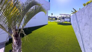A modern building with a white exterior and blue accents, a well-maintained lawn, and a clear sky. - Villa 6- Pink Princess (Golf Del Sur)