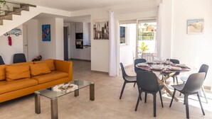 En moderne stue med en sofa, et glasbord og et spiseområde med et bord dækket til fire personer.