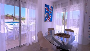 Un comedor moderno con mesa y sillas de vidrio, un cuadro en la pared y vista a una piscina exterior.