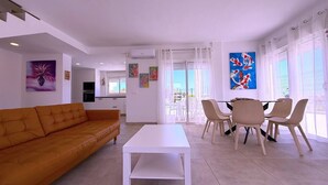 Una sala de estar moderna con una mesa de centro blanca, sofá naranja y un comedor con sillas color beige.