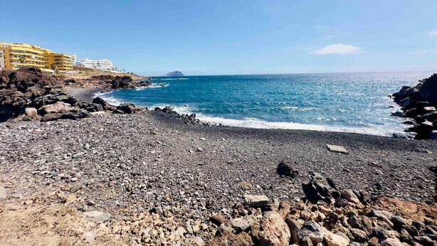Una playa rocosa con vistas despejadas al océano y una isla distante.