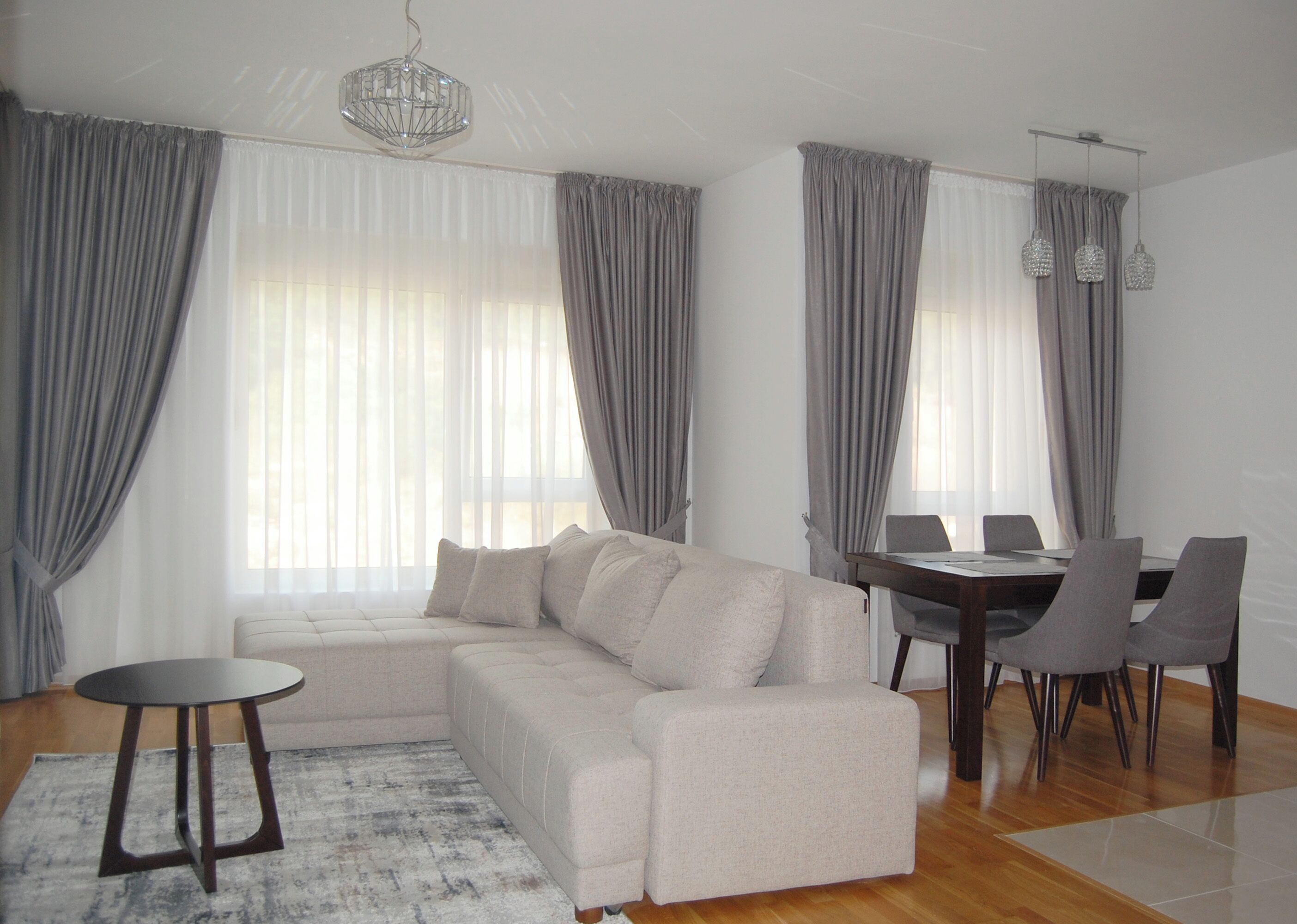 Una sala moderna con un sofá modular, una mesa de comedor con sillas y una araña.