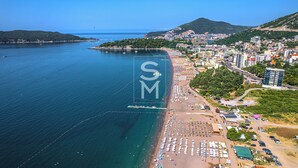 An aerial view of a coastal city with a beach, buildings, and a hilly landscape. - Status Apartments 100 (Becici)