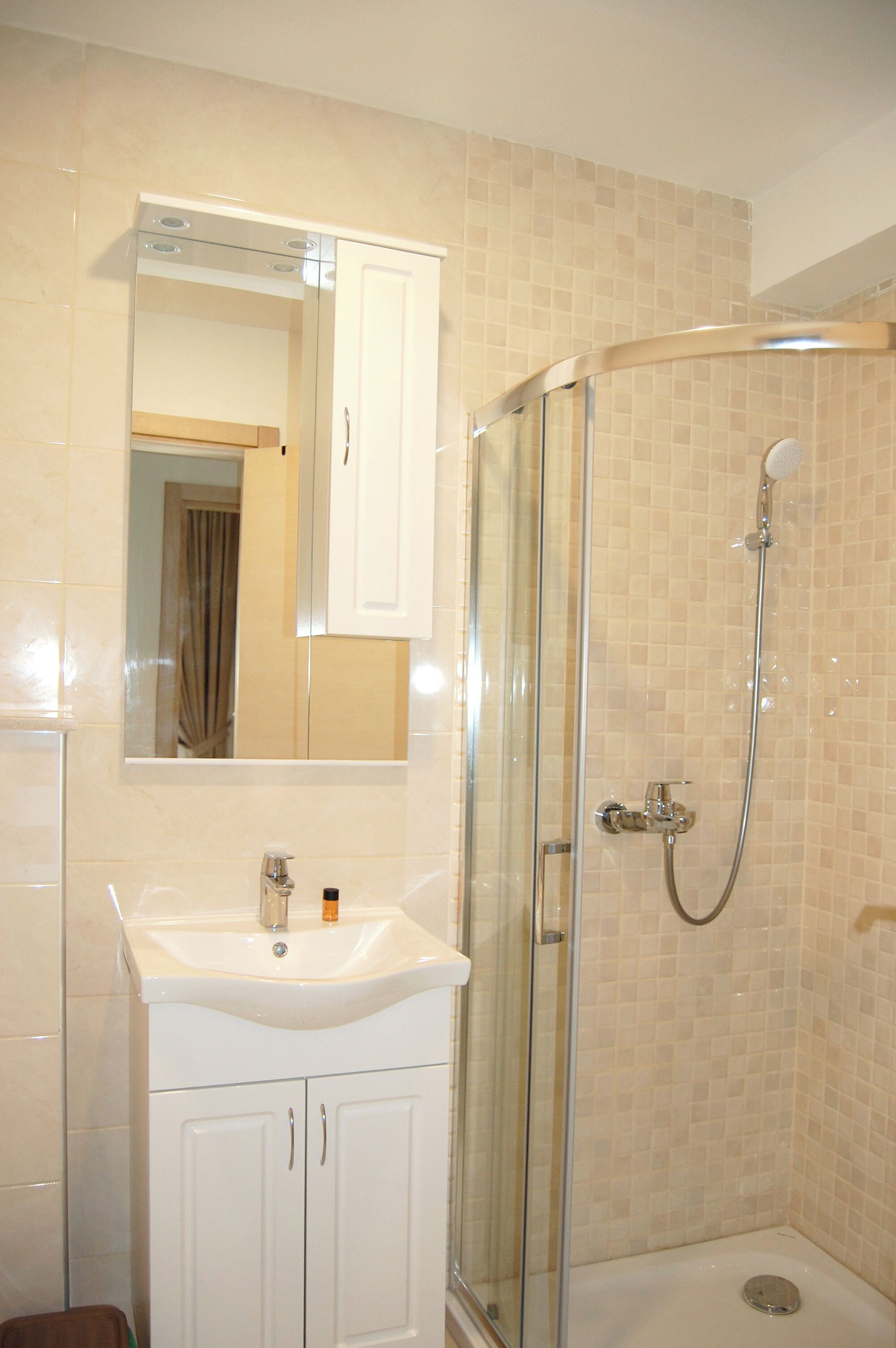 A bathroom with a glass-enclosed shower, a white sink, and a mirror above it.