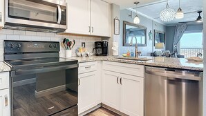 Una cocina moderna con armarios blancos, lavavajillas de acero inoxidable, horno empotrado, microondas y cafetera.