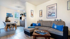 Ein Wohnzimmer mit einer Couch, einem Esstisch und einer Küche im Hintergrund.