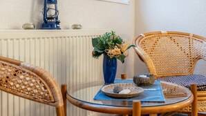 Ein runder Glastisch mit Korbstühlen, eine blaue Vase mit Grünpflanzen und ein kleines dekoratives Objekt darauf.