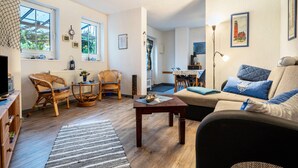 Ein Wohnzimmer mit Sofa, Sesseln, einem Couchtisch und einem Essbereich im Hintergrund.