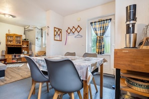 Uma sala de jantar com mesa posta para quatro pessoas, uma televisão e um armário de madeira com copos.