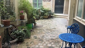 Un cortile con pavimento in pietra, piante in vaso e sedie e tavoli in metallo blu.