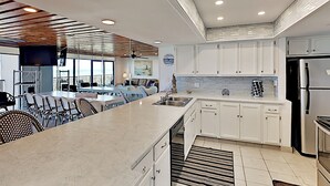 Una cocina moderna con armarios blancos, una isla grande con asientos y vista al océano.