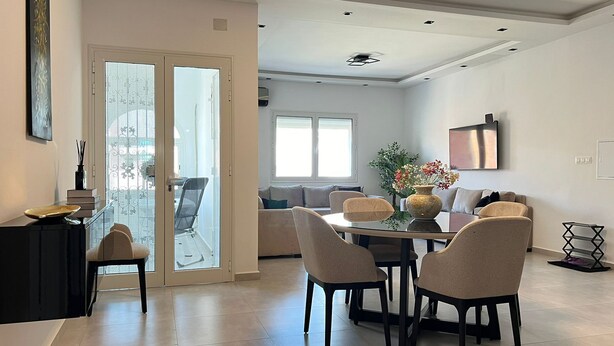 A modern dining area with a glass table and chairs, a vase with flowers, and a sofa in the background. - New York meets Hergla! Fantastic modern vacation apartment near the beach (Hergla)