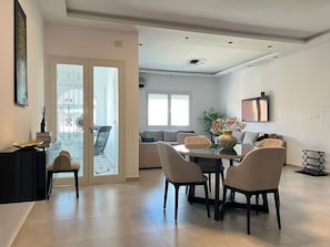 Un comedor moderno con una mesa y sillas de vidrio, un jarrón con flores y un sofá al fondo.