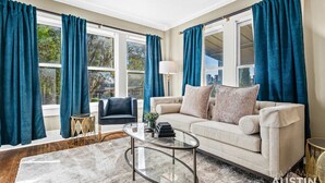 A living room with a beige sofa, a glass coffee table, and teal curtains. - Pet-Friendly East Austin Home w Free Parking & Grill│Walk to 6th & Rainey (Austin)