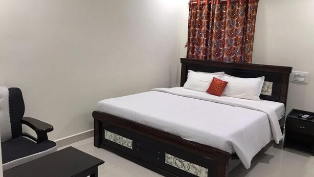 A bedroom with a bed, a chair, a table, and an air conditioning unit. - Sri Kamakshi Bhavan (Narayanavanam)