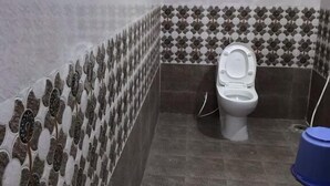A bathroom with a toilet, patterned tiles, and a blue trash bin. - Sri Kamakshi Bhavan (Narayanavanam)