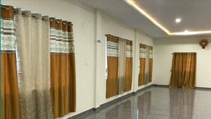 A hotel corridor with a polished floor, curtains on the windows, and a ceiling fan. - Sri Kamakshi Bhavan (Narayanavanam)