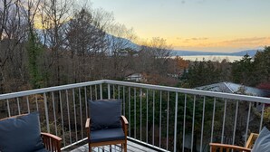 A wooden deck with two chairs and a railing overlooking a forested area with a distant mountain range.