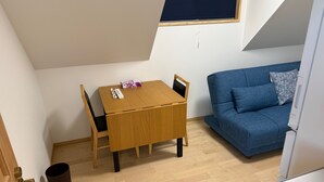 Ein kleiner, gut beleuchteter Raum mit einem Holztisch und -stühlen, einem blauen Sofa und einem Fenster mit dunkler Jalousie.
