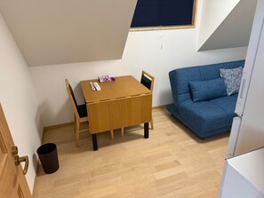 Una habitación pequeña y bien iluminada con una mesa y sillas de madera, un sofá azul y una ventana con una persiana oscura.