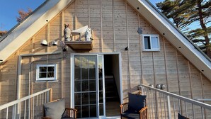 Eine Holzhütte mit Balkon, einer Schiebetür aus Glas und zwei Holzstühlen.