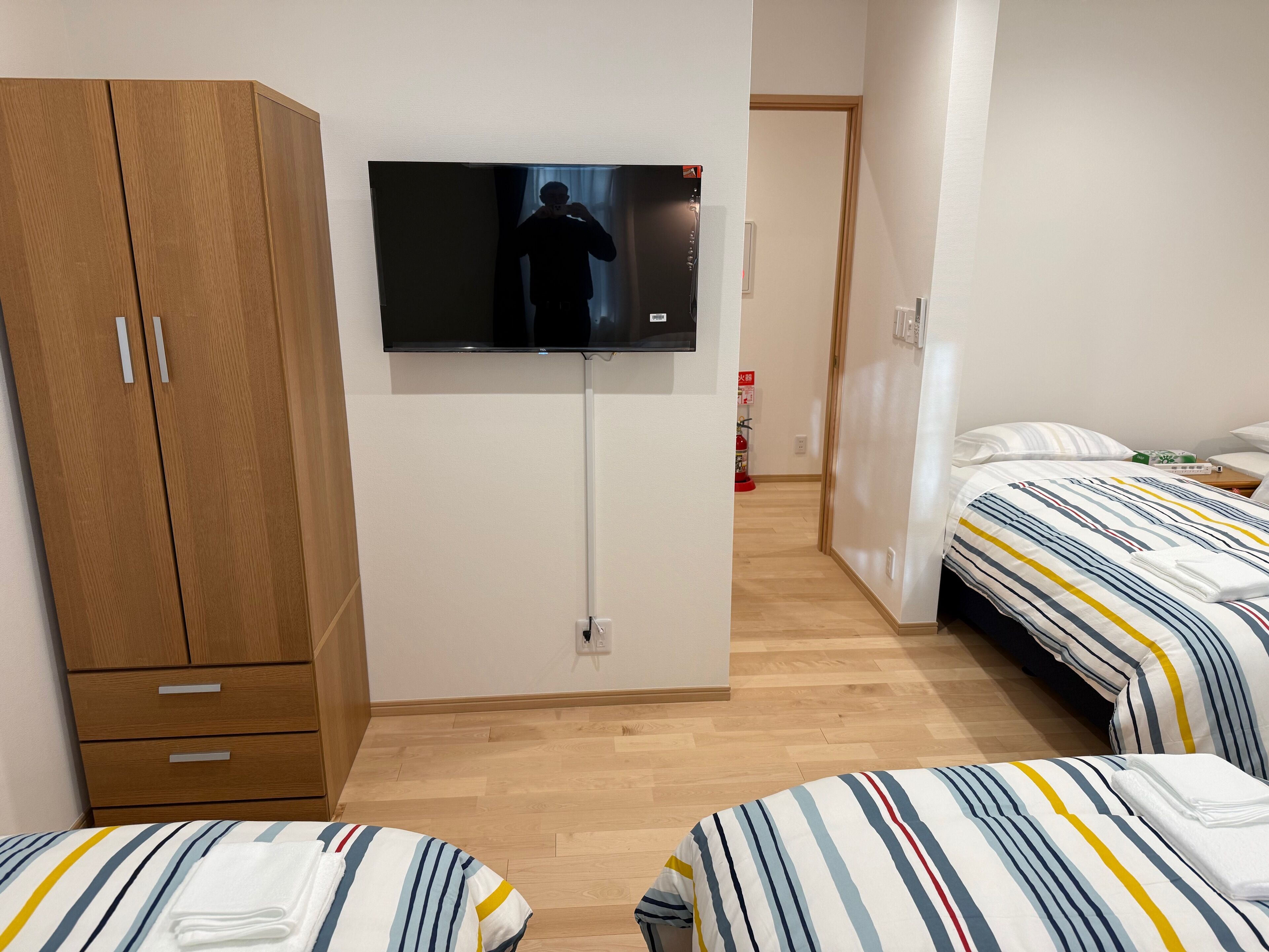 Ett hotellrum med två sängar, en TV som är monterad på väggen, ett träskåp och en brandsläckare i hallen.